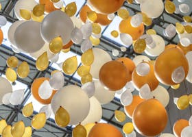Vibrant arrangement of orange, white, and yellow balloons hanging in an indoor celebration space.